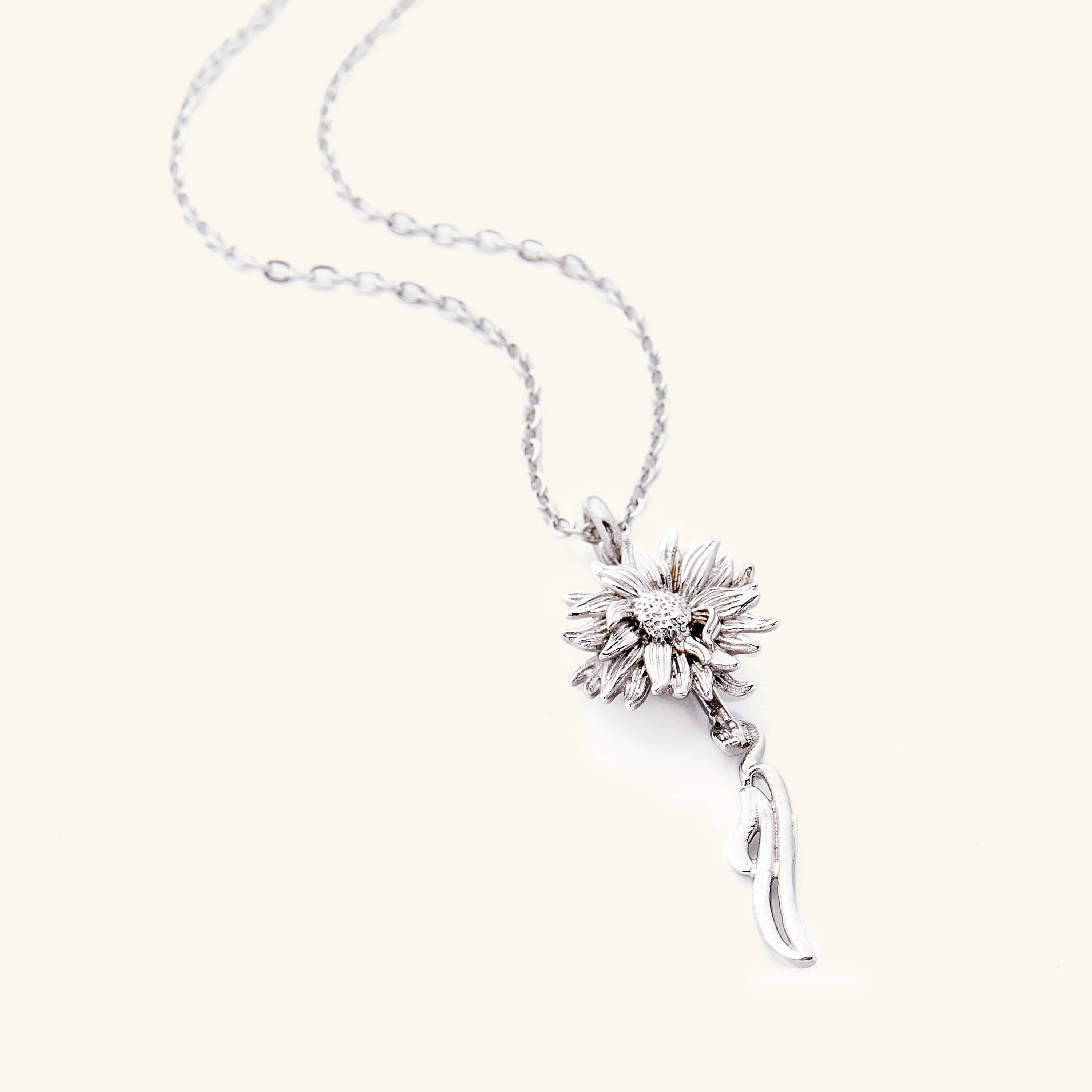 A silver necklace that features a sunflower shaped pendant with Arabic word for ‘happiness’, curving in calligraphy out of the stem of the flower