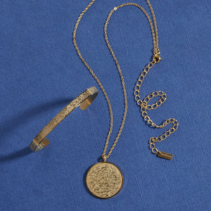 Photo of the gold Ayatul Kursi necklace and Ayatul Kursi Cuff against a blue background.