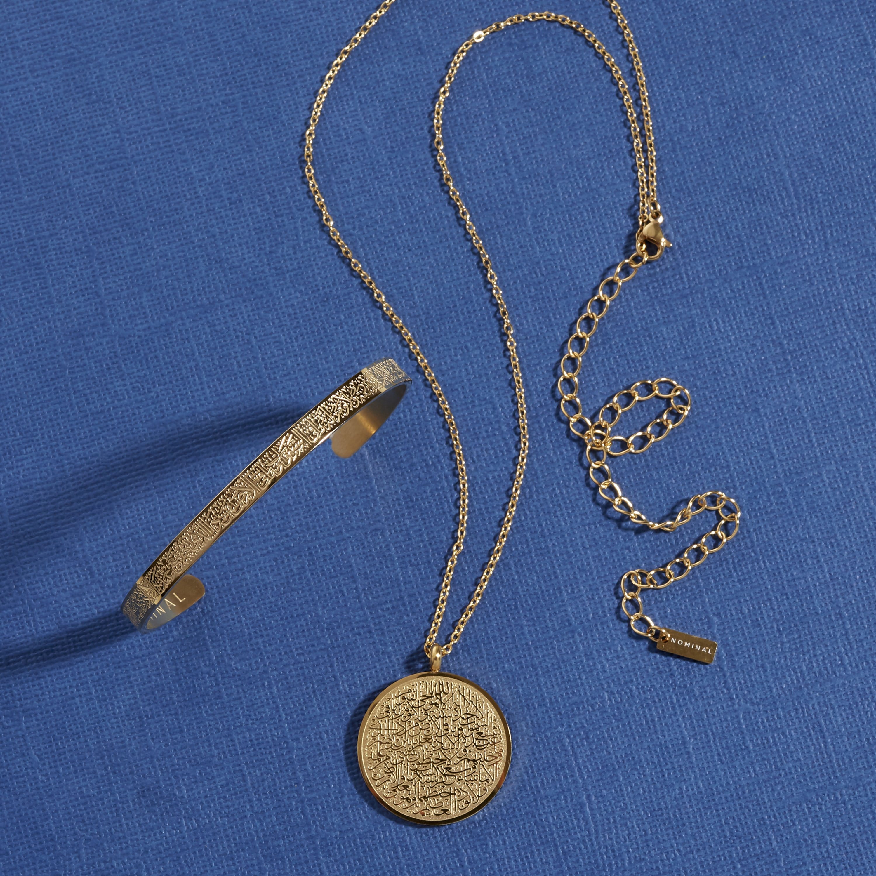 Photo of the gold Ayatul Kursi necklace and Ayatul Kursi Cuff against a blue background.