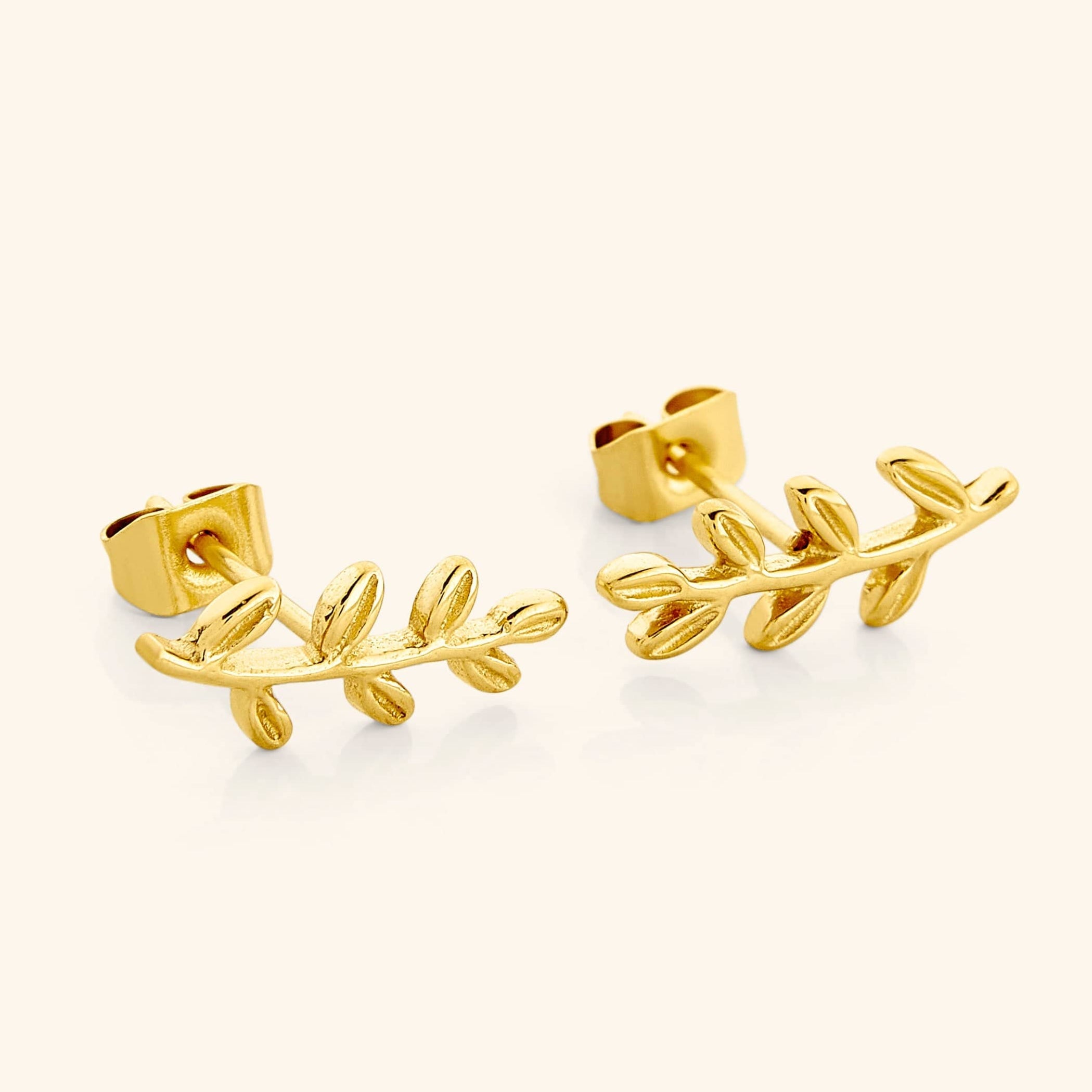 A close-up of the Olive Leaf Earrings in 18K gold plating. The earrings feature delicate olive leaf designs, symbolizing resilience and connection, suspended from hypoallergenic stainless steel posts.