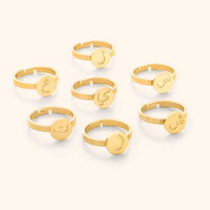 Seven gold rings displayed flat lay, each with a round face engraved in Arabic letters