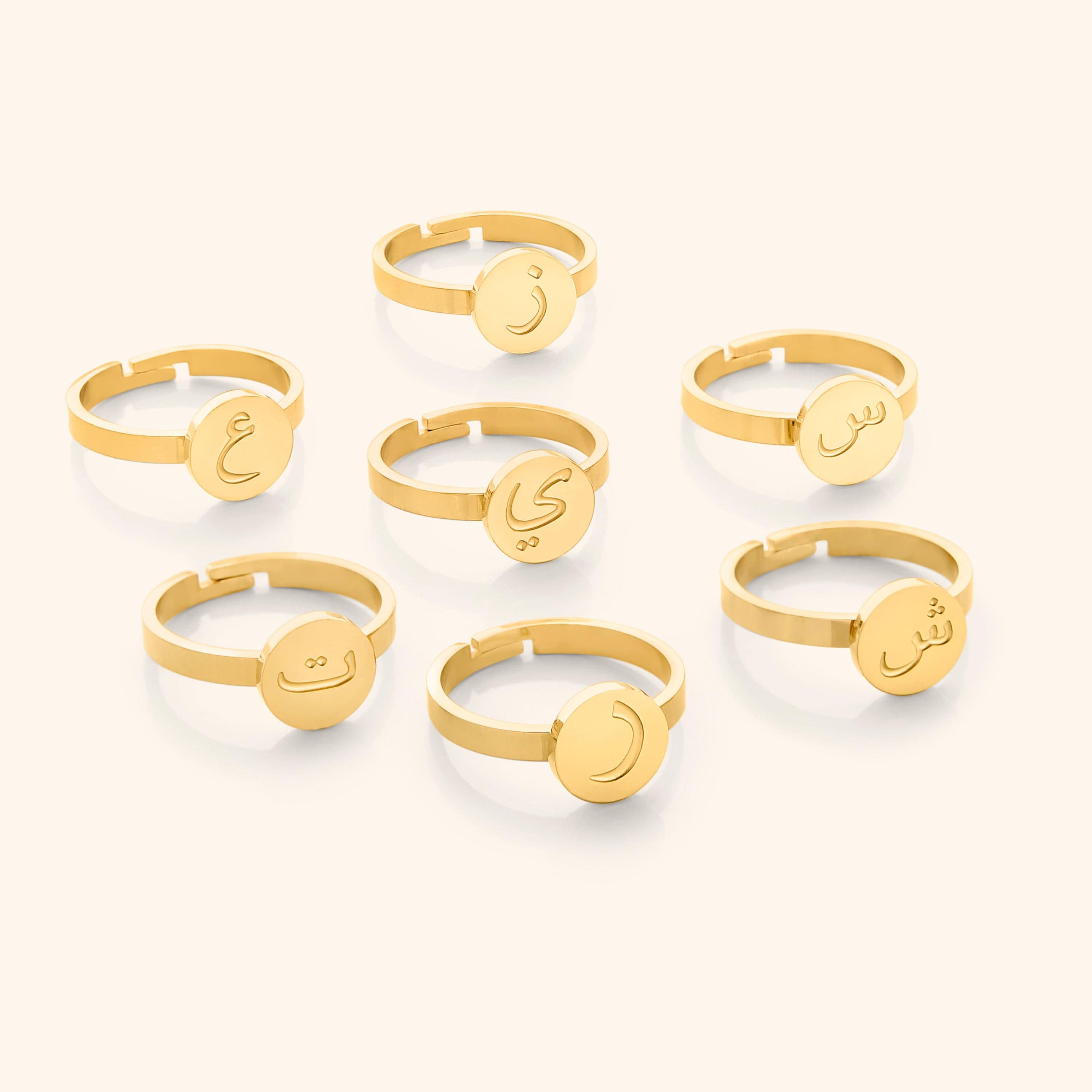 Seven gold rings displayed flat lay, each with a round face engraved in Arabic letters