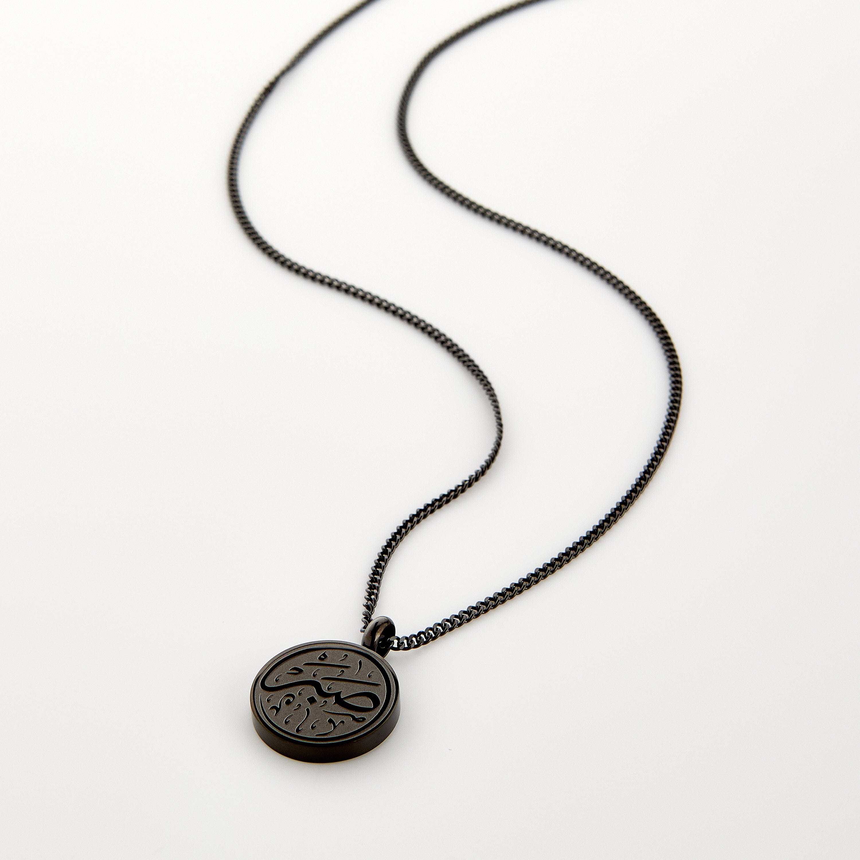 Black necklace with a circular 'Sabr' calligraphy engraved pendant, displayed on a white background.