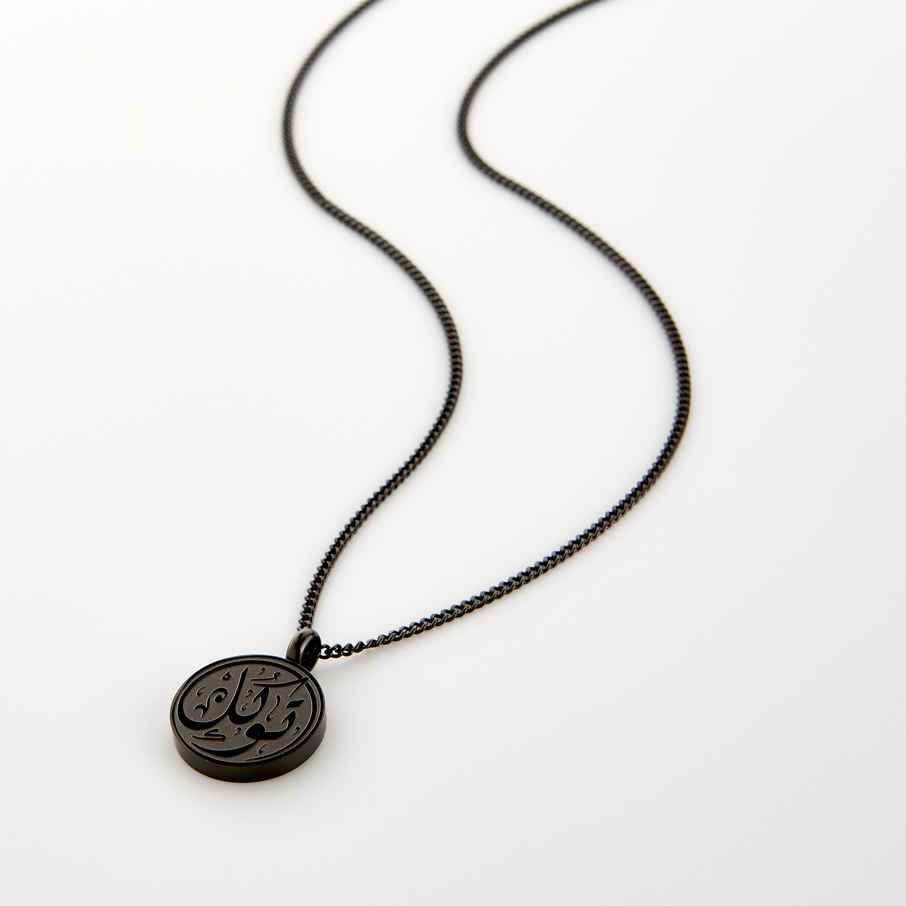 Black necklace with a circular pendant engraved with 'Tawakkul' calligraphy, displayed on a white background.