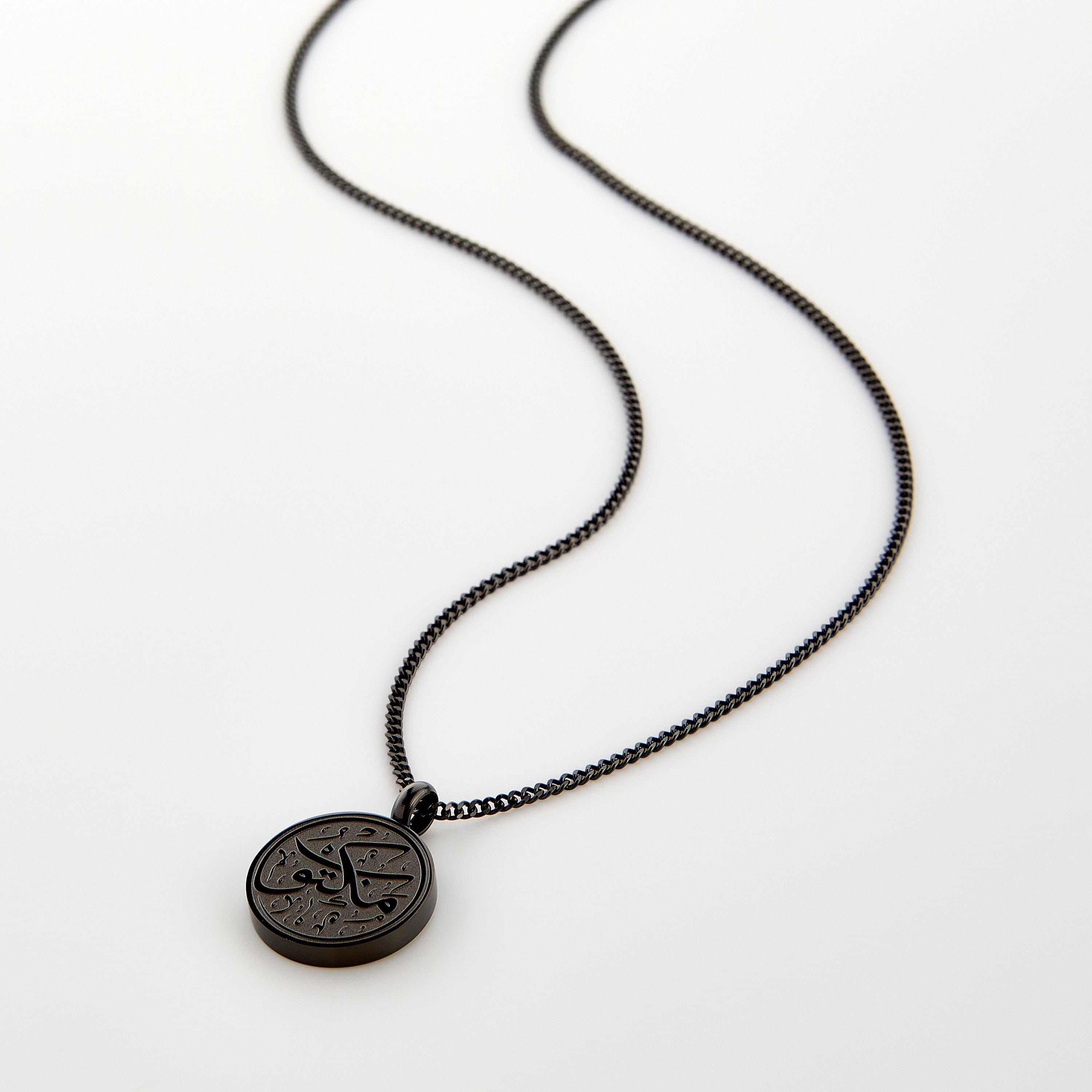 Black necklace with a circular pendant engraved with 'Maktub' calligraphy, displayed on a white background.