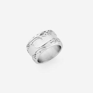 A silver thick ring that features an iconic line from Rumi carved into a wide band: "The wound is where the light enters you." The center of the ring is smooth and traced floral details along the edges.