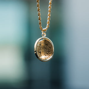 Close-up of a gold  car hanger with a circular pendant engraved in Arabic calligraphy of the Shahada.