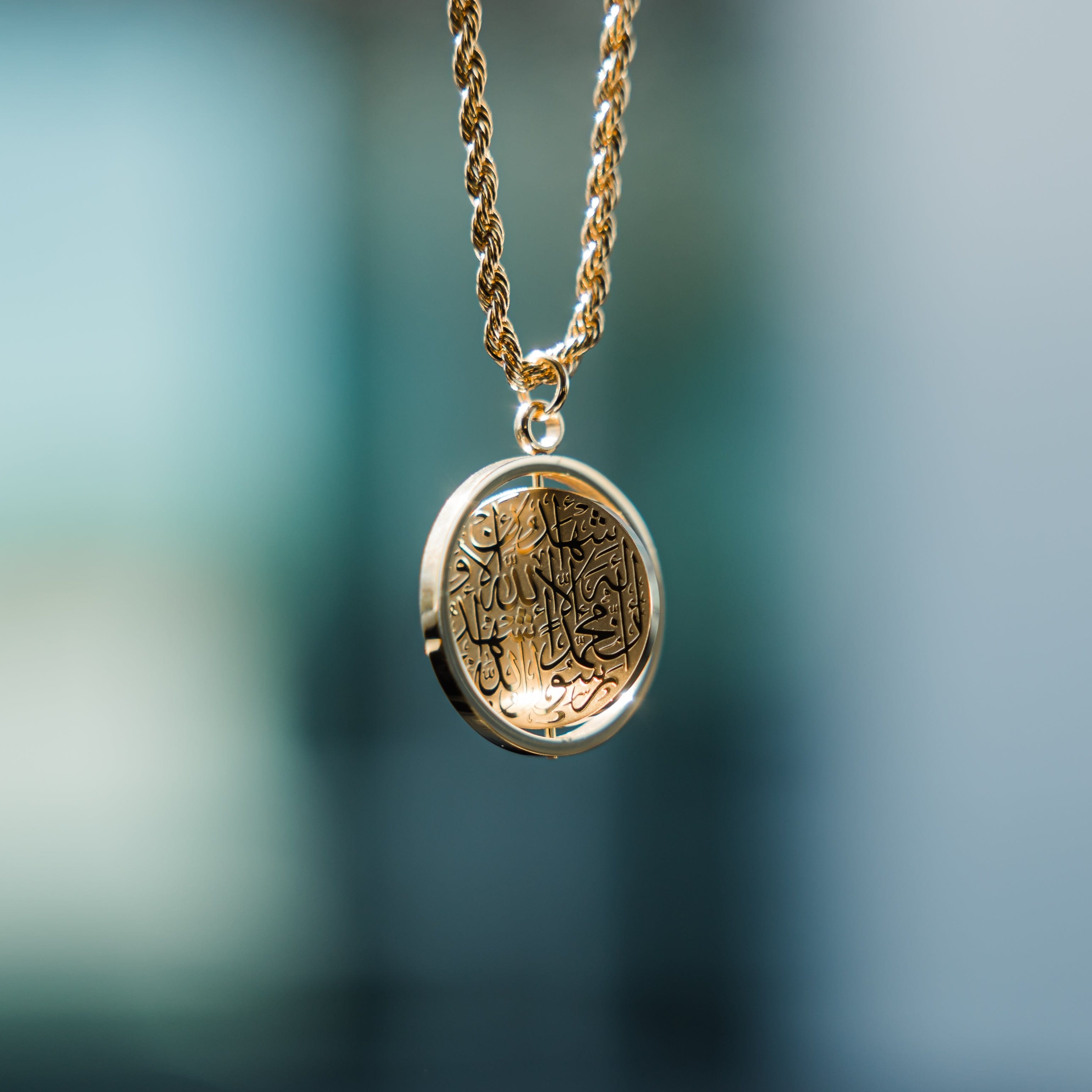 Close-up of a gold  car hanger with a circular pendant engraved in Arabic calligraphy of the Shahada.