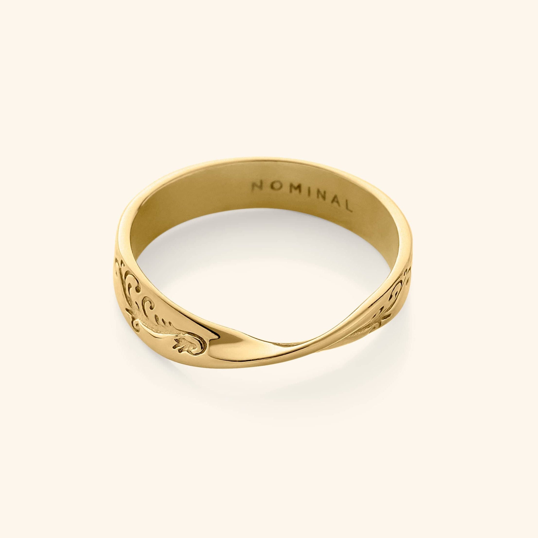 Close-up of a gold band ring engraved with swirling wave-like patterns, featuring a twist at the center.