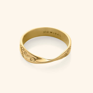 Close-up of a gold band ring engraved with swirling wave-like patterns, featuring a twist at the center.