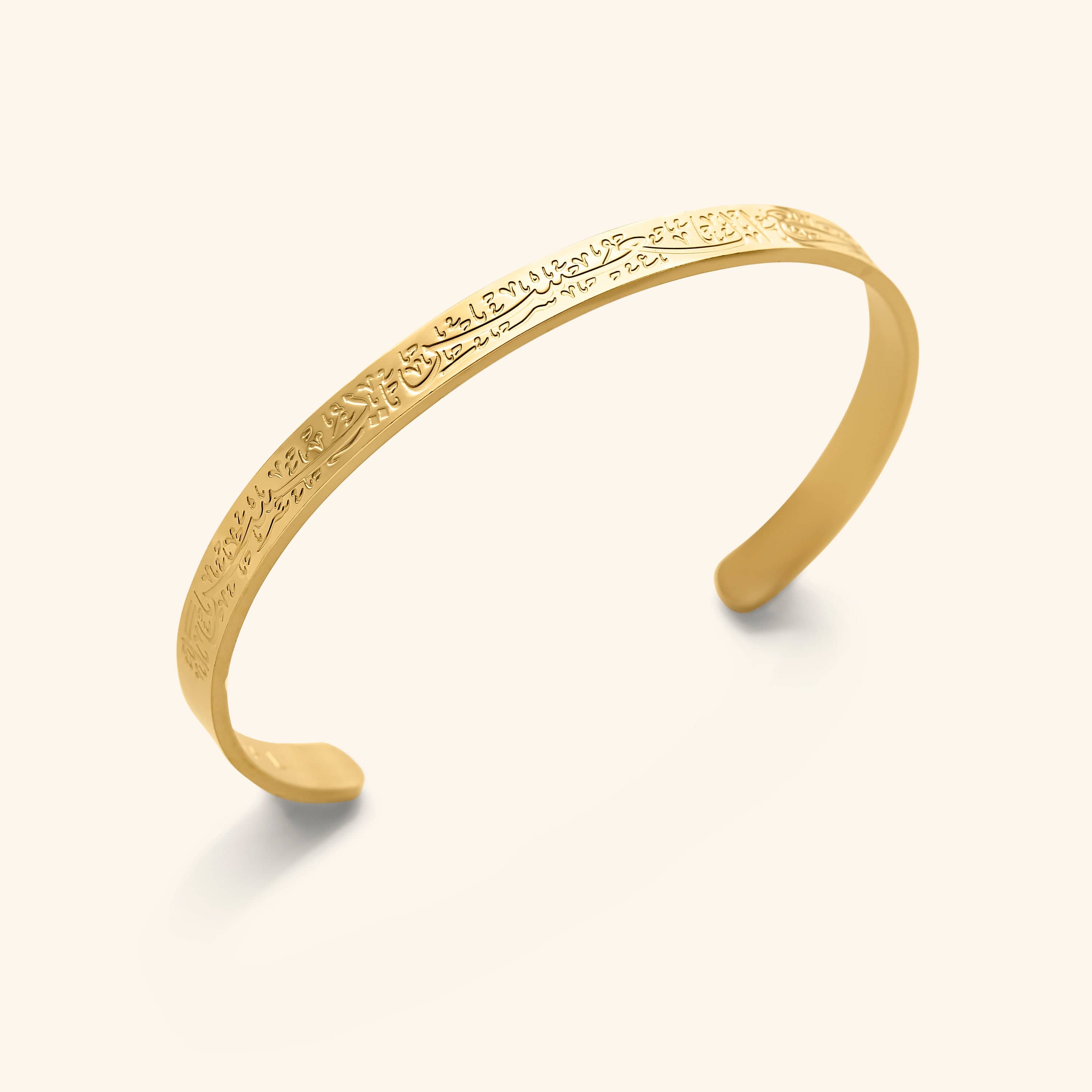 A close-up of the "With Hardship Comes Ease" Cuff V2 in 18K gold plating. The cuff features an embossed Arabic calligraphy inscription: "إِنَّ مَعَ الْعُسْرِ يُسْرًا" ("Verily, with every hardship comes ease") from Quran 94:5-6. The design is elegant and minimalist, suitable for daily wear.