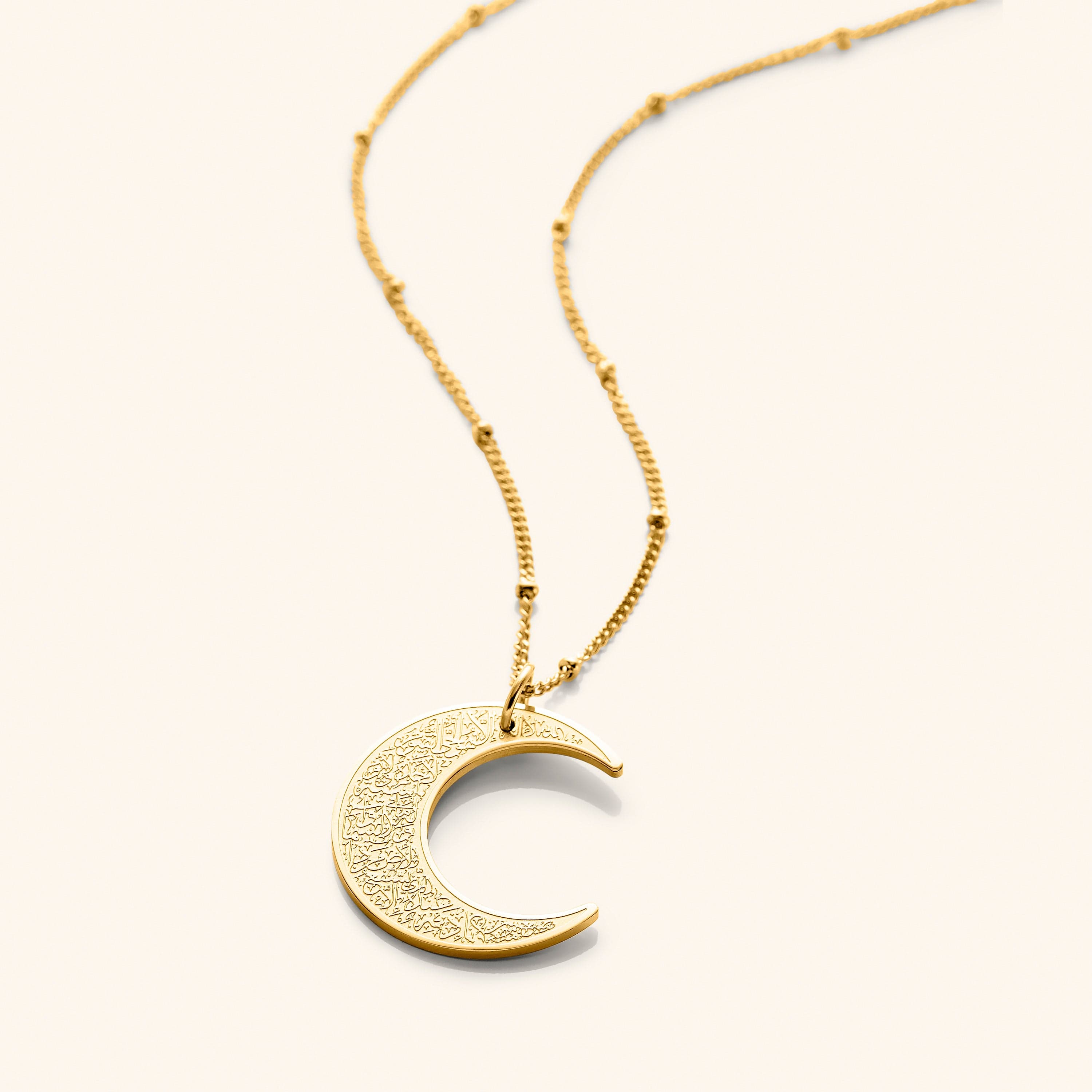 A close-up of the Ayatul Kursi Crescent Necklace in 18K gold plating, featuring a crescent-shaped pendant intricately engraved with Arabic calligraphy, suspended from a delicate cable chain.