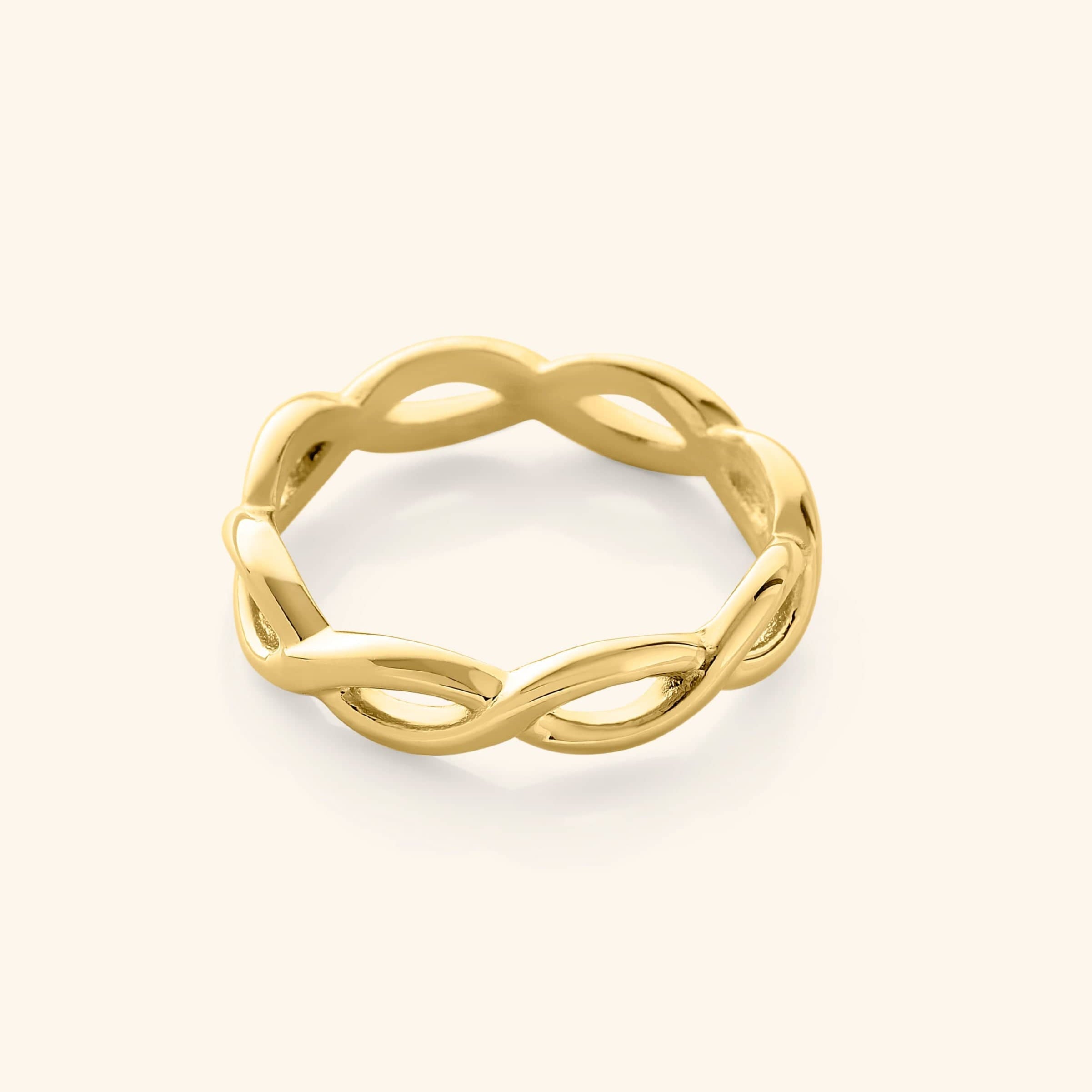 Gold infinity ring with a continuous twisted loop design, photographed against a neutral beige background.