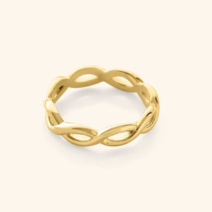 Gold infinity ring with a continuous twisted loop design, photographed against a neutral beige background.