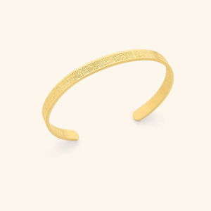 Photo of the 18k gold plated 4 Qul Cuff against a light background.This piece features the four surahs beginning with "Qul" separated with a slight gap on the cuff, engraved on the front and back.