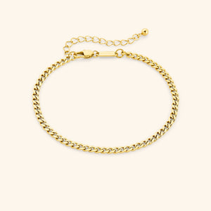 Chunky gold curb chain anklet with lobster clasp and extender, tag engraved with "NOMINAL" visible near the clasp, laid out on a soft beige surface.