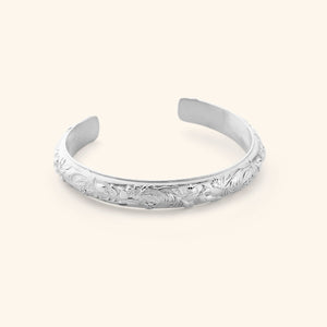 A silver cuff etched with jasmine, marigolds, and water lilies art.