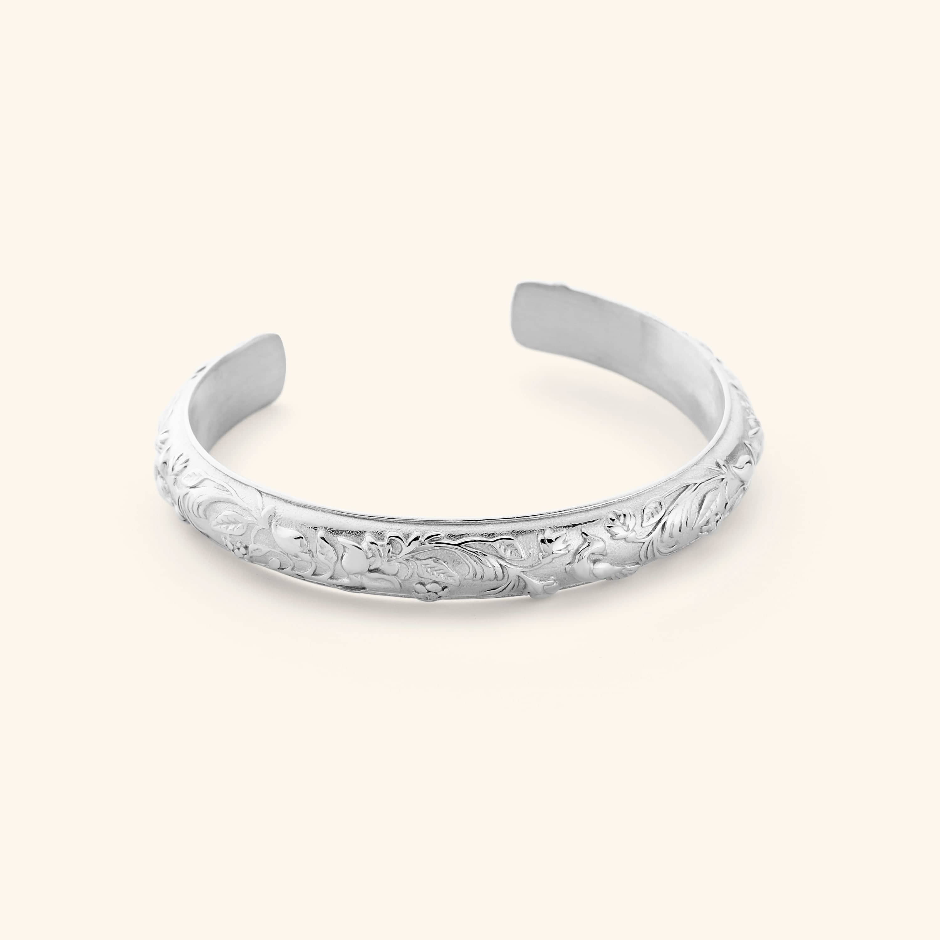 A silver cuff etched with jasmine, marigolds, and water lilies art.