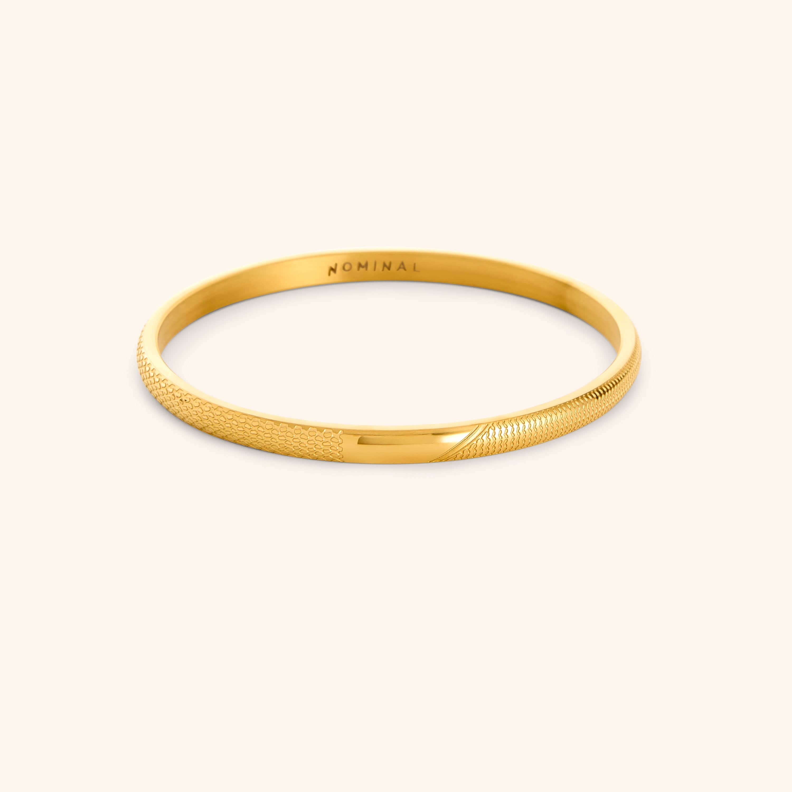 Gold keffiyeh pattern engraved bangle with 'NOMINAL' branding on a light background.
