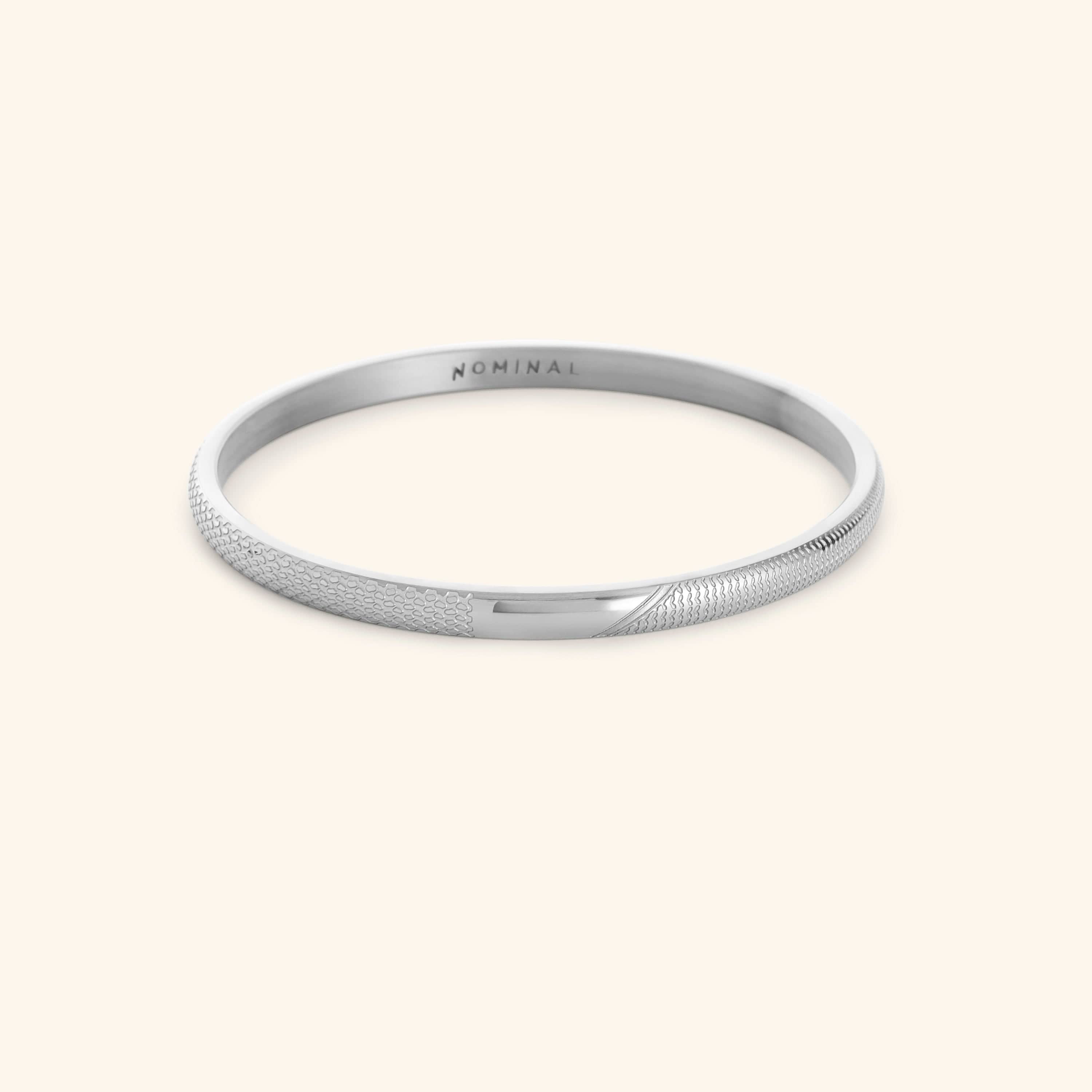 Silver keffiyeh pattern engraved bangle with NOMINAL branding on a light background.