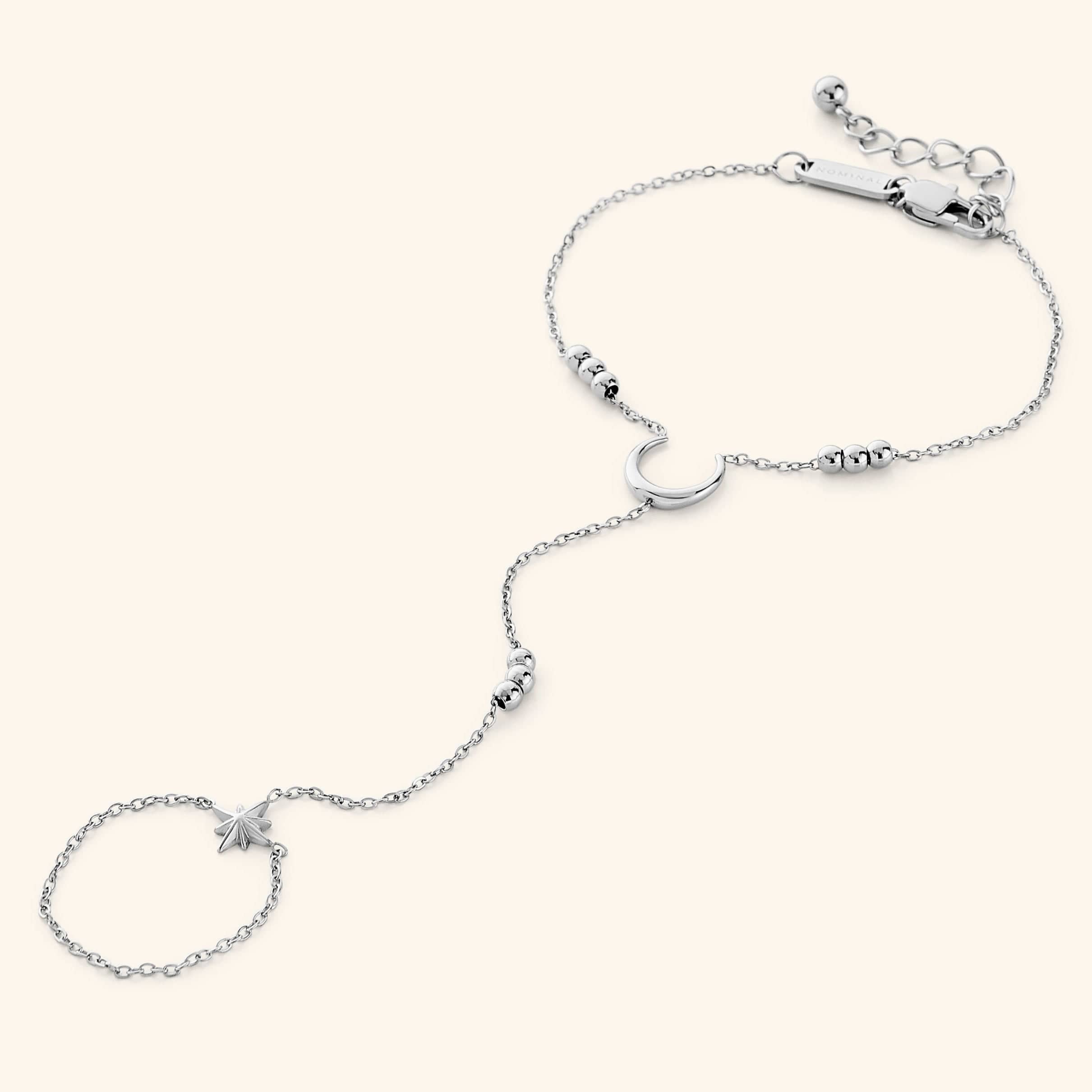 Silver lunar handchain featuring a delicate chain design with a crescent moon centerpiece, bead accents, and a small star charm connected to a finger loop, displayed on a neutral background.