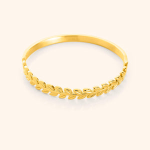 A close-up of the Palestine Olive Layering Bangle in 18K gold plating. The bangle features a delicately twisted olive branch design along one half, symbolizing peace and strength, while the other half remains sleek and unadorned for a modern balance.