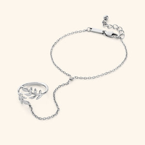 The Shining Olive Hand Chain in a silver finish. The hand chain showcases a delicate chain connecting a ring with an olive leaf design to a bracelet.