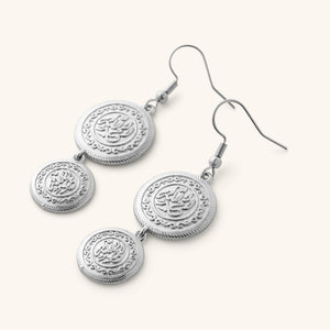 A pair of silver earrings that features feature Arabic calligraphy embossed into the coins.