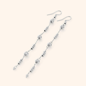 Flat lay of the silver earrings. Comet Earrings drop 3.5 inches with delicate, evenly spaced orbs.