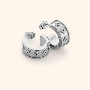Flat lay of silver Henna Hoops, wide curved band with raised dotted floral motifs on a textured background.