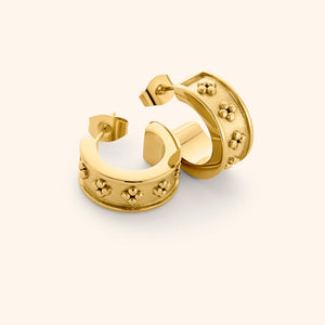 Flat lay of gold Henna Hoops, featuring wide curved band with raised dotted floral motifs on a textured surface.