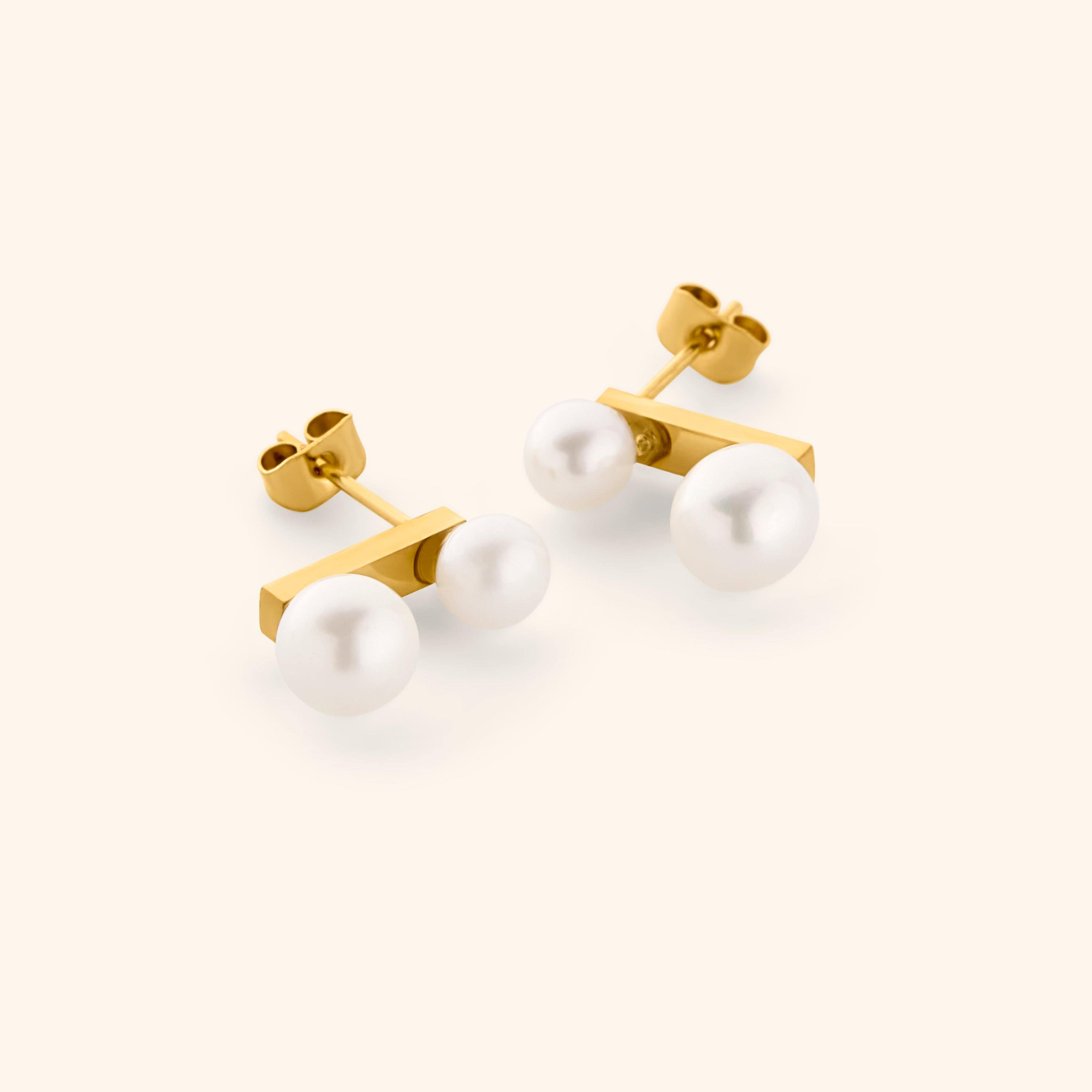 Gold stud earrings with two different sized pearls, shot on a light background