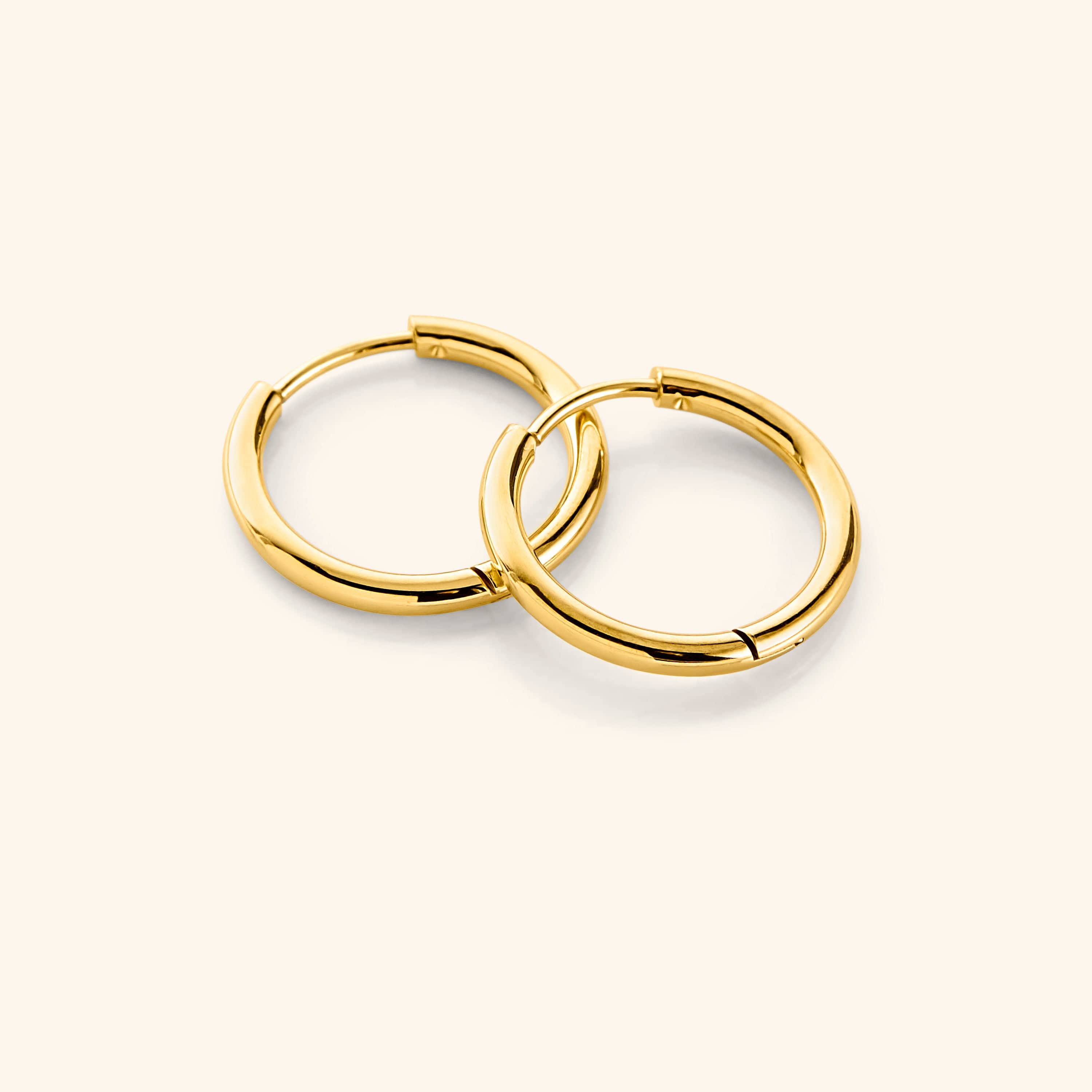 Flat lay of the 18K gold plated Small Essential Hoops | 14mm against a light background.