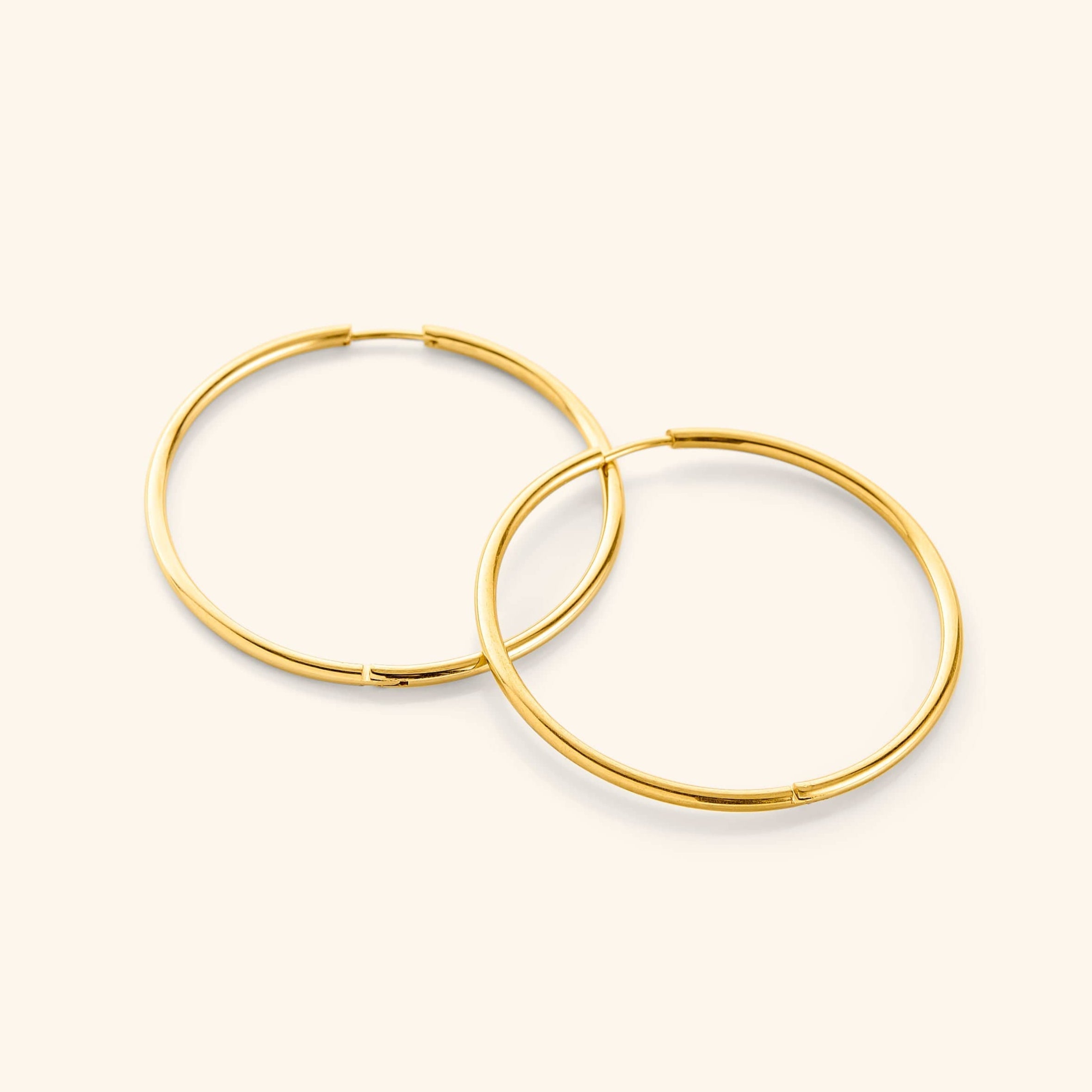 Flat lay of a pair of 18k gold plated Oversized Essential Hoops | 40mm against a light background.