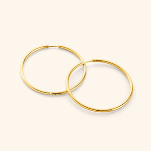 Flat lay of a pair of 18k gold plated Oversized Essential Hoops | 40mm against a light background.