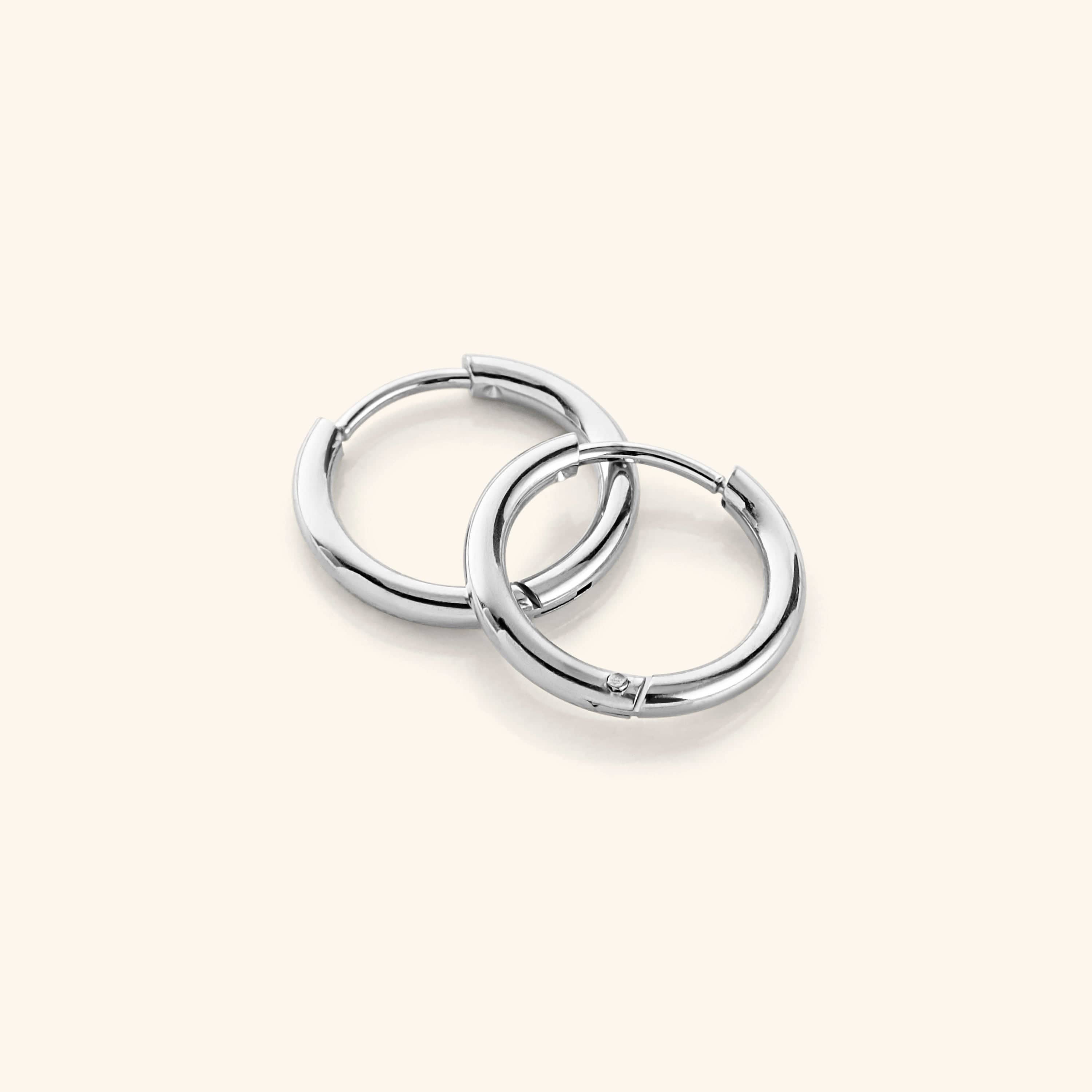 a pair of silver Huggie Essential Hoops | 12mm against a light background.