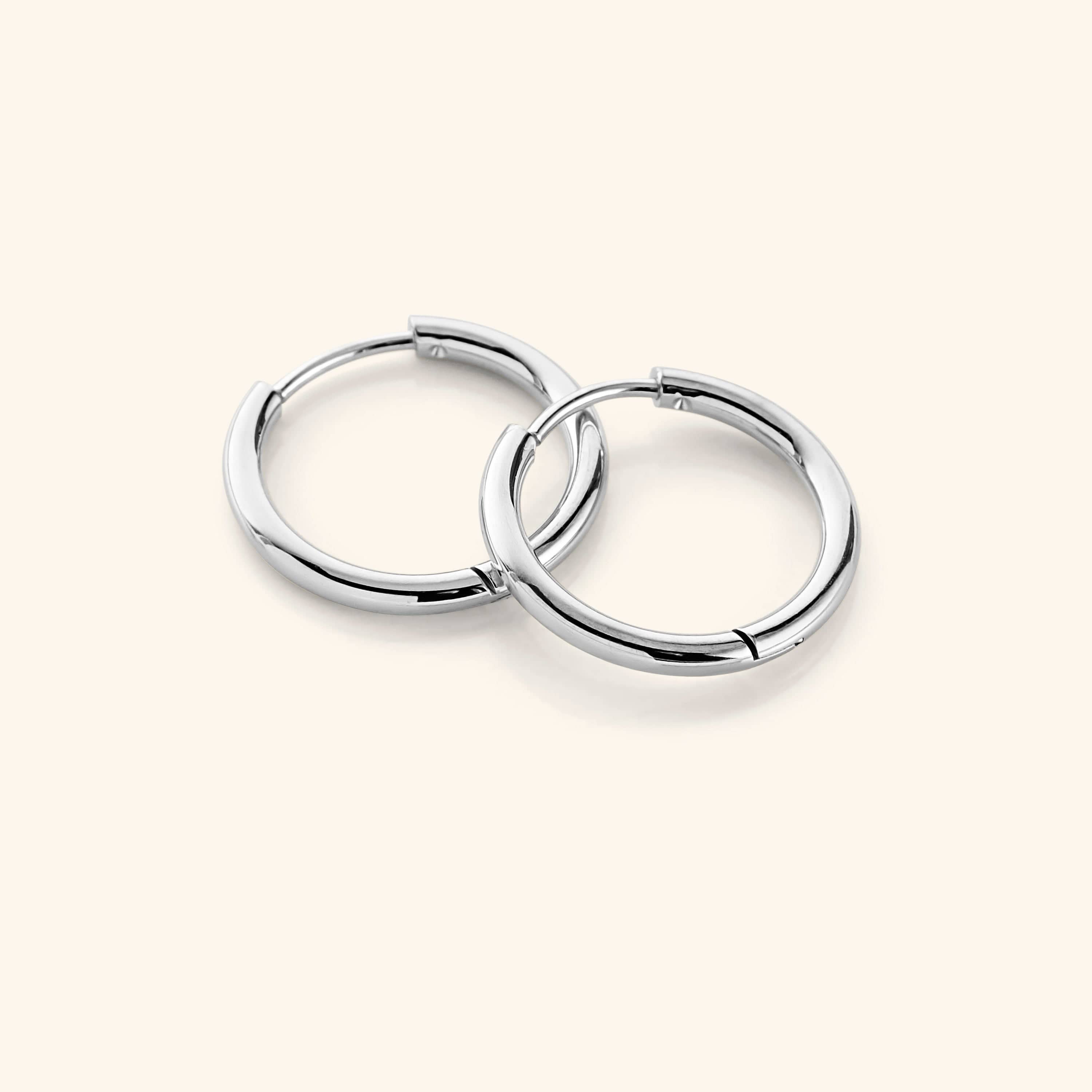 Flat lay of the silver Small Essential Hoops | 14mm against a light background.