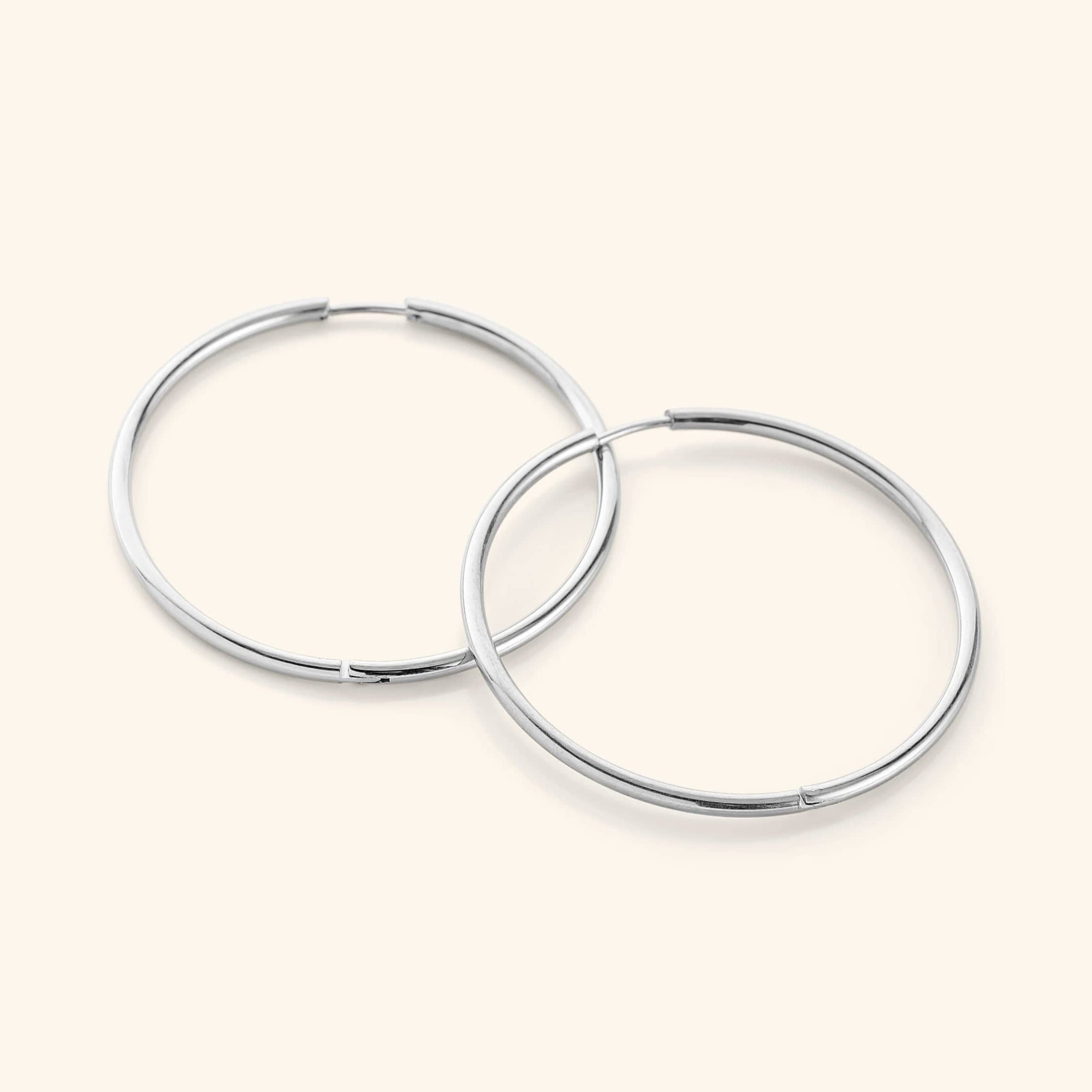 Flat lay of a pair of silver Oversized Essential Hoops | 40mm against a light background.