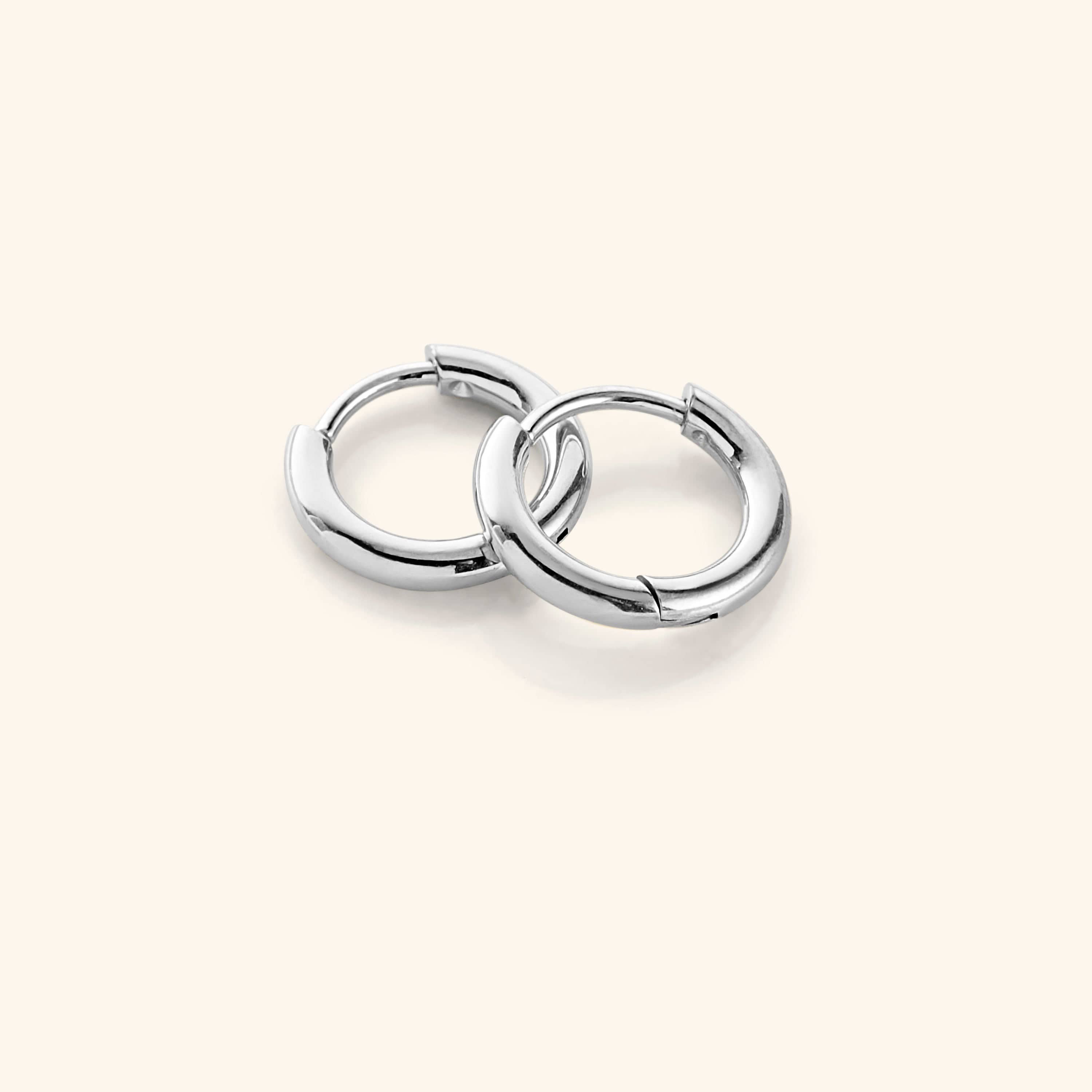 Flat lay of the silver Huggie Essential Hoops | 8mm against a white background.