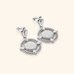 A pair of silver dangling earrings that features the  "perhaps you dislike what's good for you" in Arabic calligraphy engraved at the center of the beaded coin. 