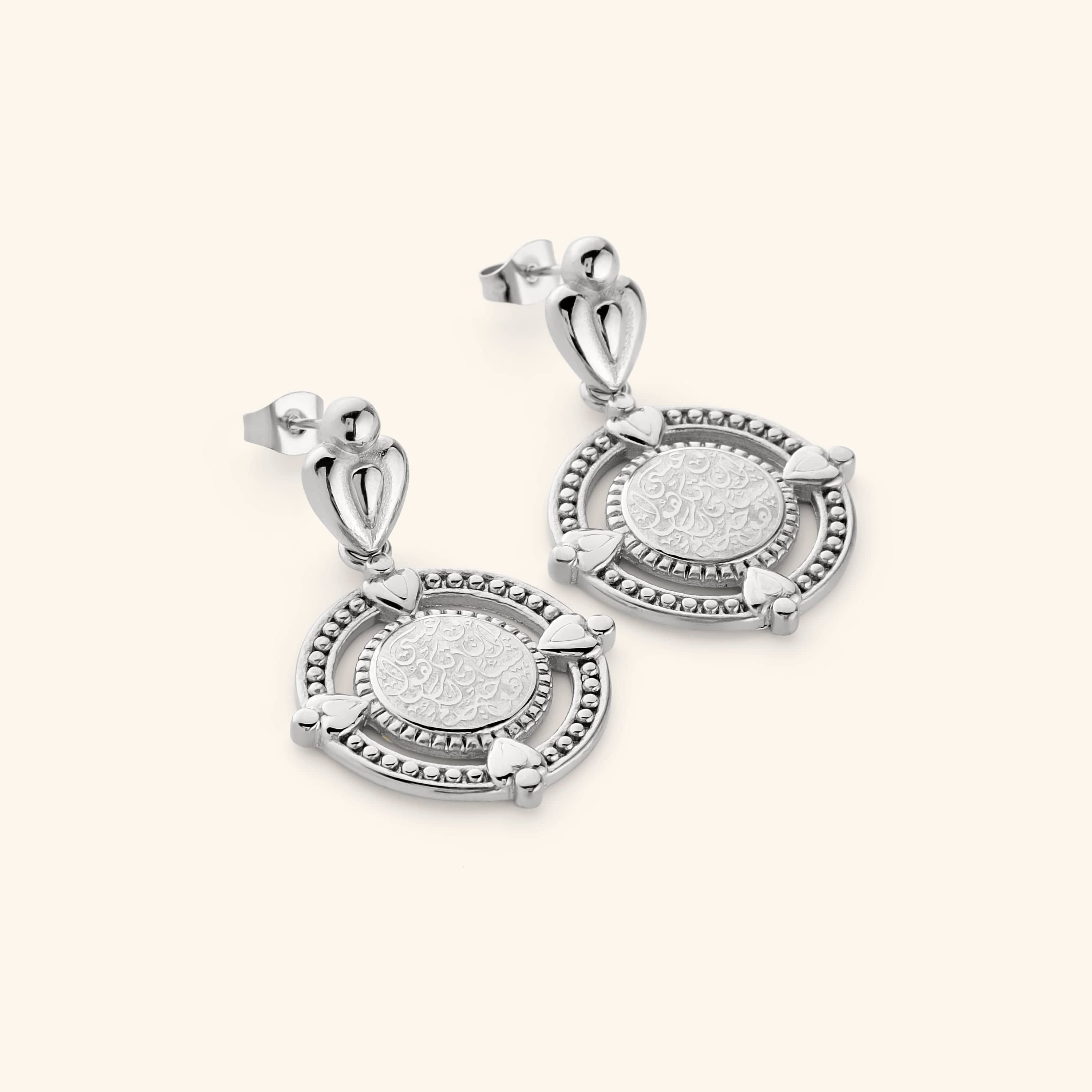 A pair of silver dangling earrings that features the  "perhaps you dislike what's good for you" in Arabic calligraphy engraved at the center of the beaded coin. 