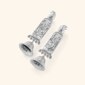 A pair of silver statement jhumkas with paisley-adorned bodies carved in floral detail, each one finished with a ridged dome beneath. 