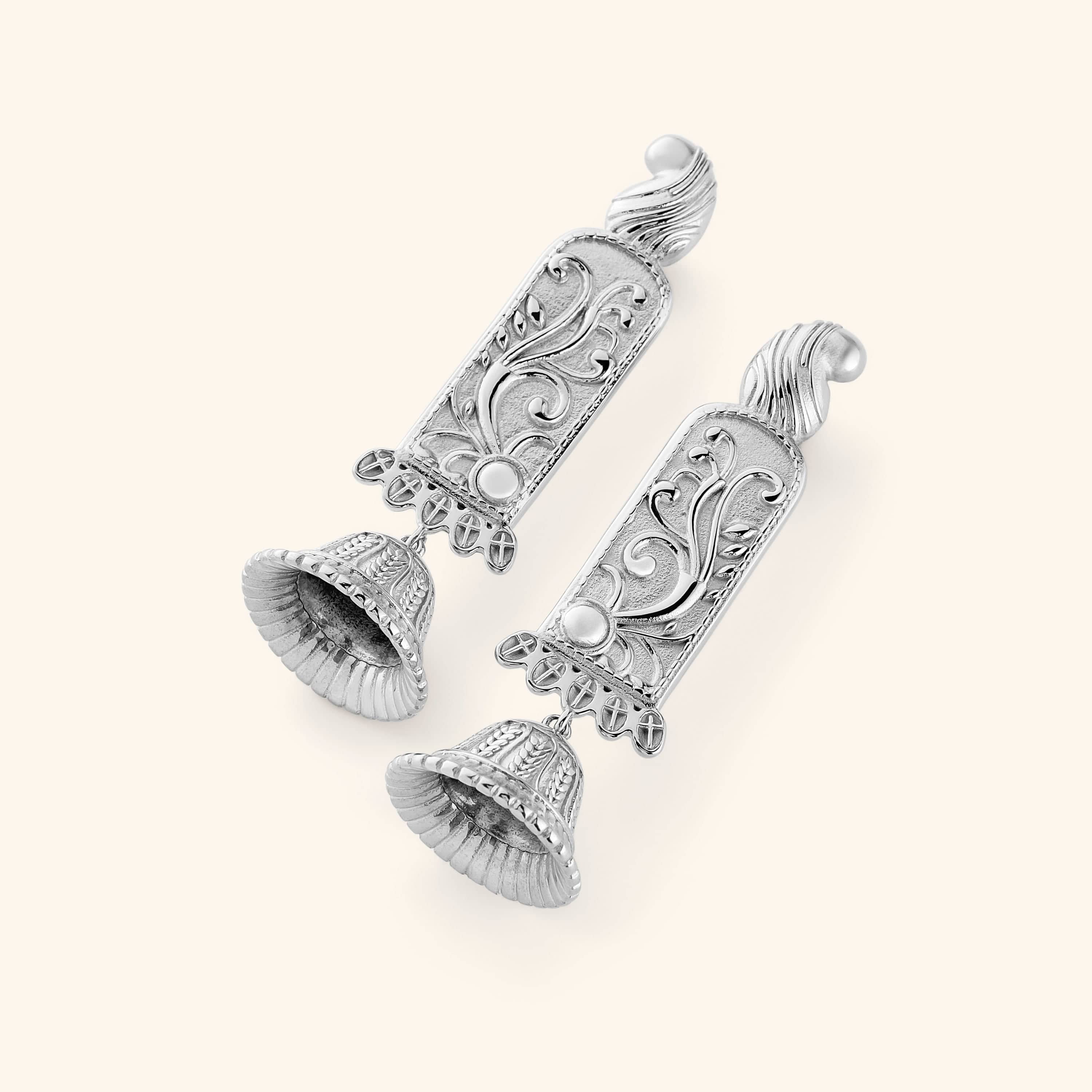A pair of silver statement jhumkas with paisley-adorned bodies carved in floral detail, each one finished with a ridged dome beneath. 