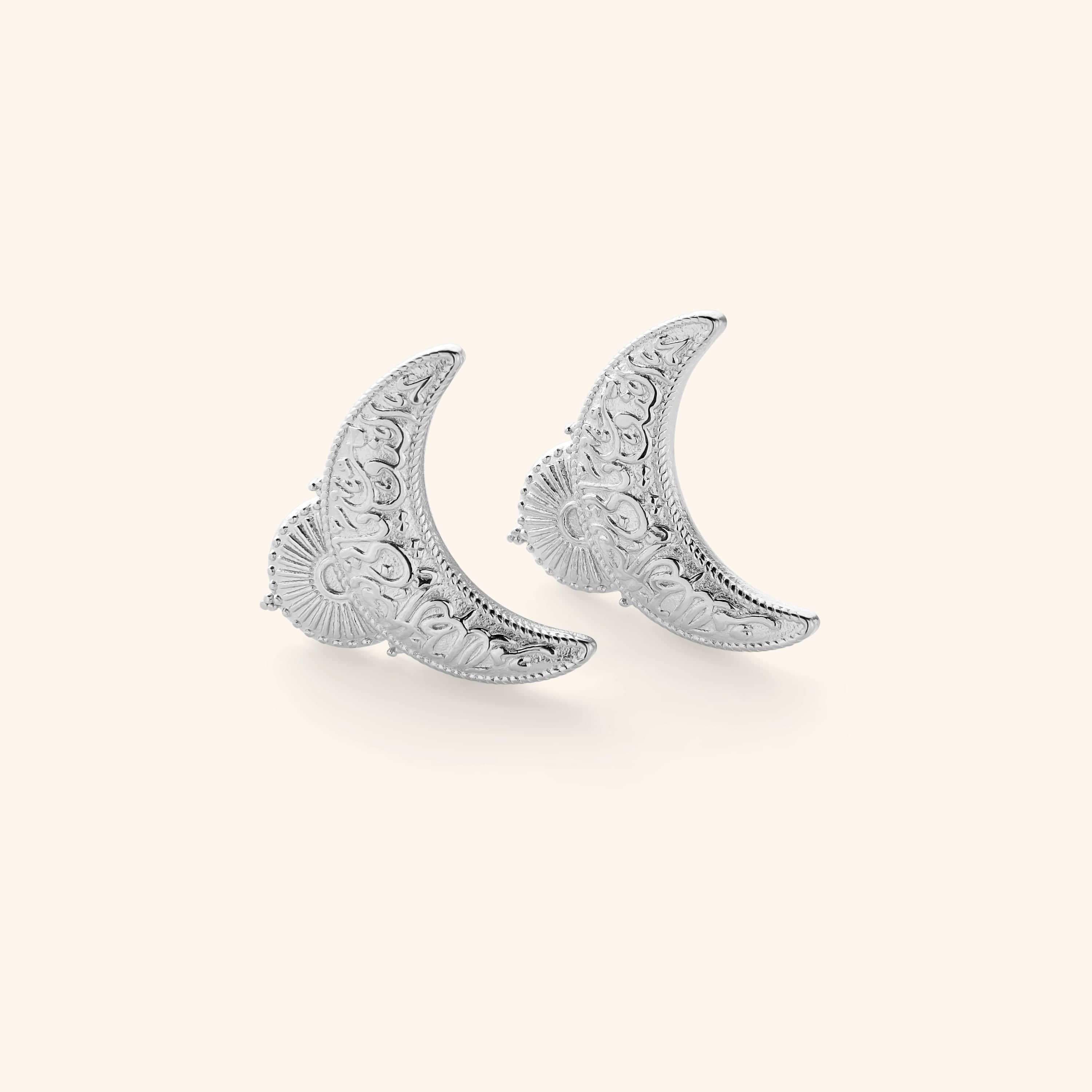Silver earrings shaped in an upside down crescent featuring an Arabic quote inscribed on each saying "light comes after darkness."