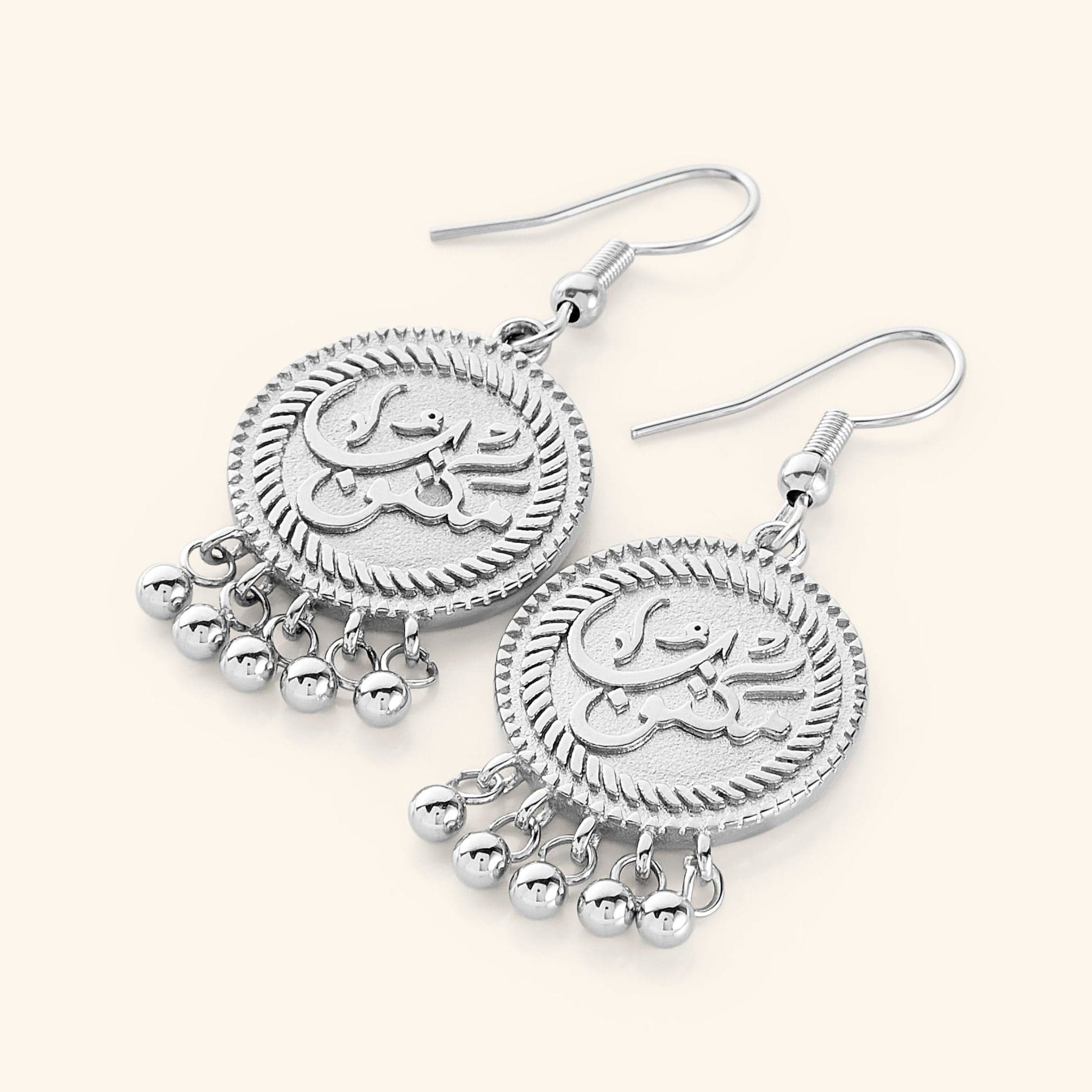 A pair of silver vintage coin earrings displayed on a white background. Each earring features a round pendant engraved with the Arabic word "مكتوب" (Maktub) and is adorned with three small dangling orbs at the bottom.
