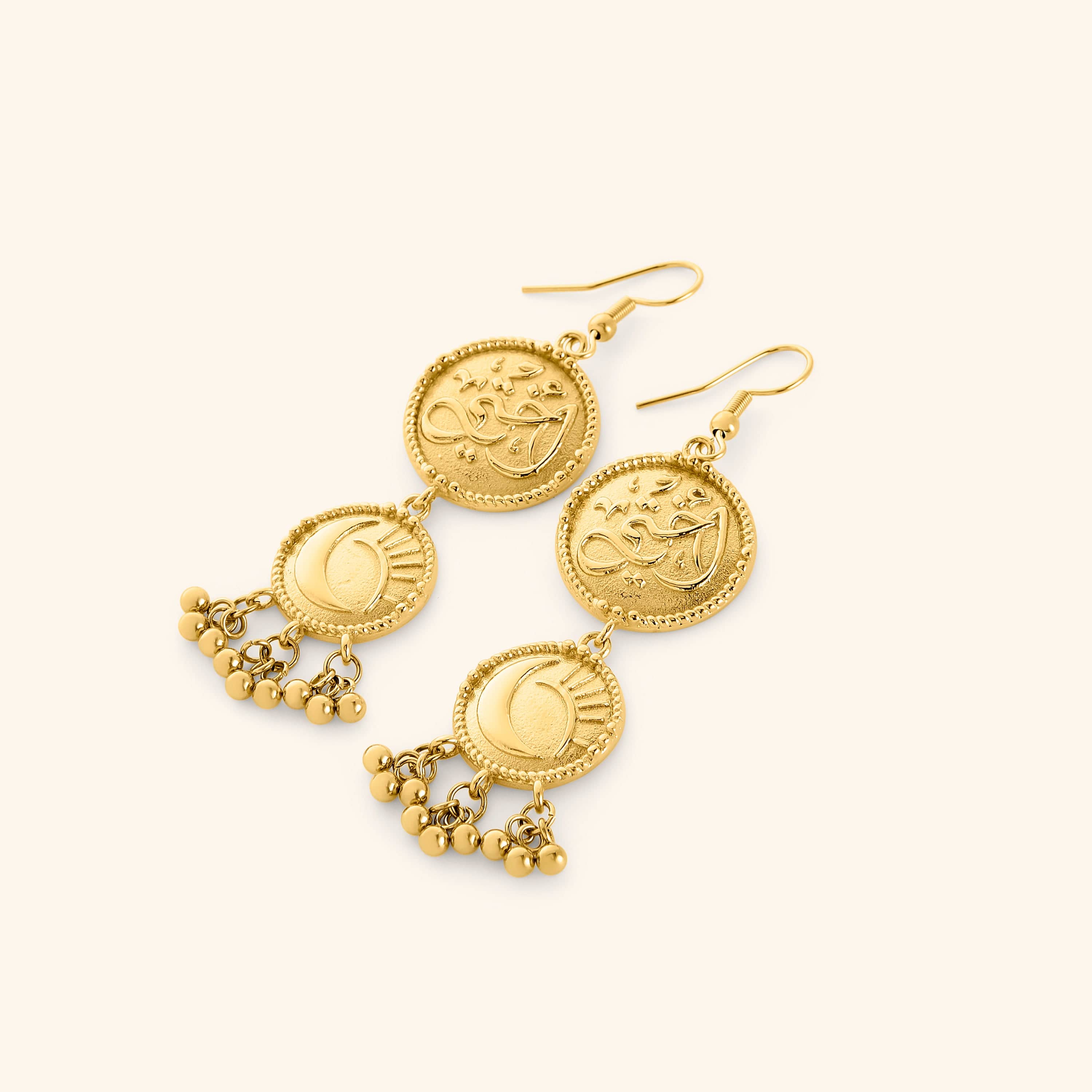 A pair of 18k gold plated dangling earrings featuring the Arabic Calligraphy of "my sister" on the first coin, dropping into a moon and star on the second coin, finished with dancing orbs.