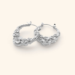 A pair of silver hoop earrings that feature sculpted poppy flower design.