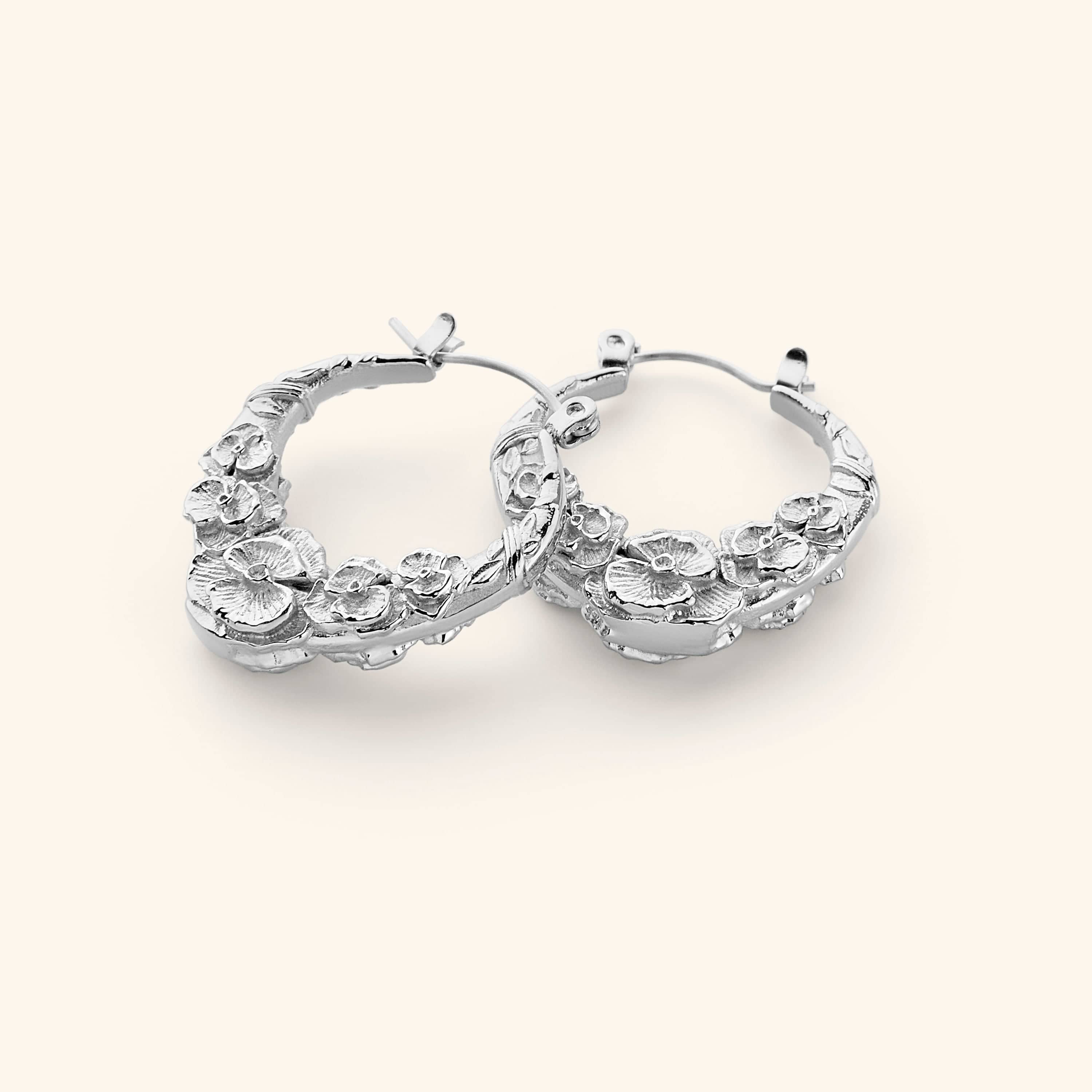A pair of silver hoop earrings that feature sculpted poppy flower design.