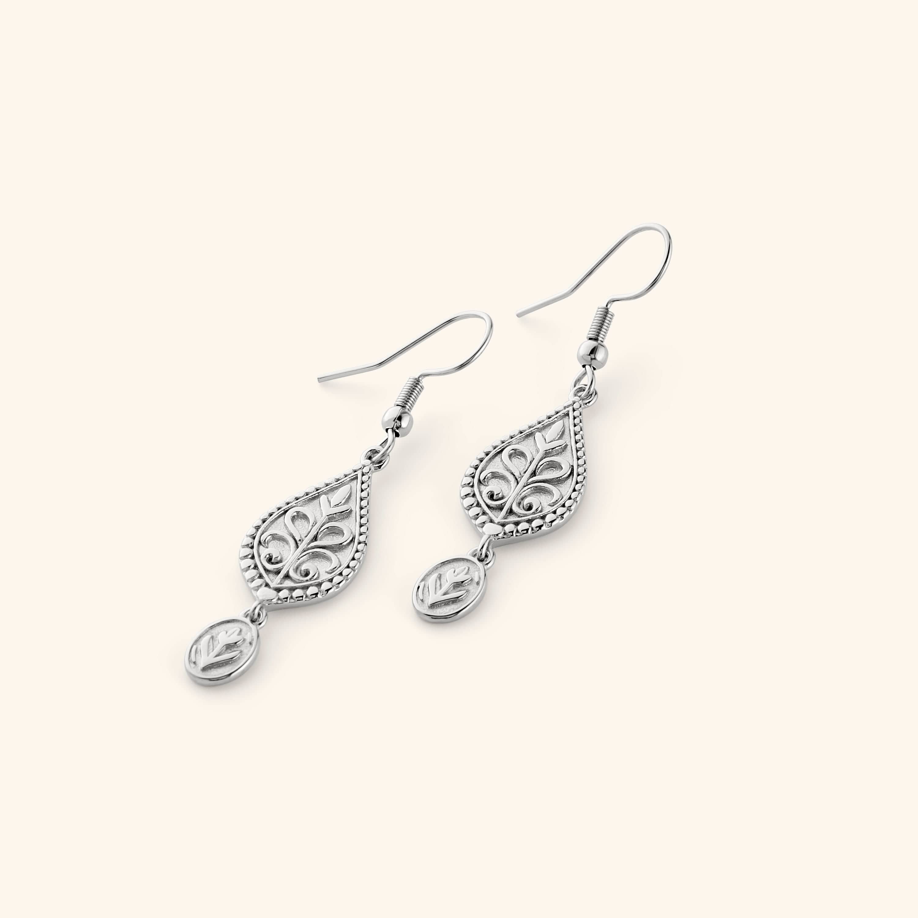 A pair of silver dangling earrings featuring Paisley droplets carved with florals and bordered in detailed beading, each one holding a small coin beneath.