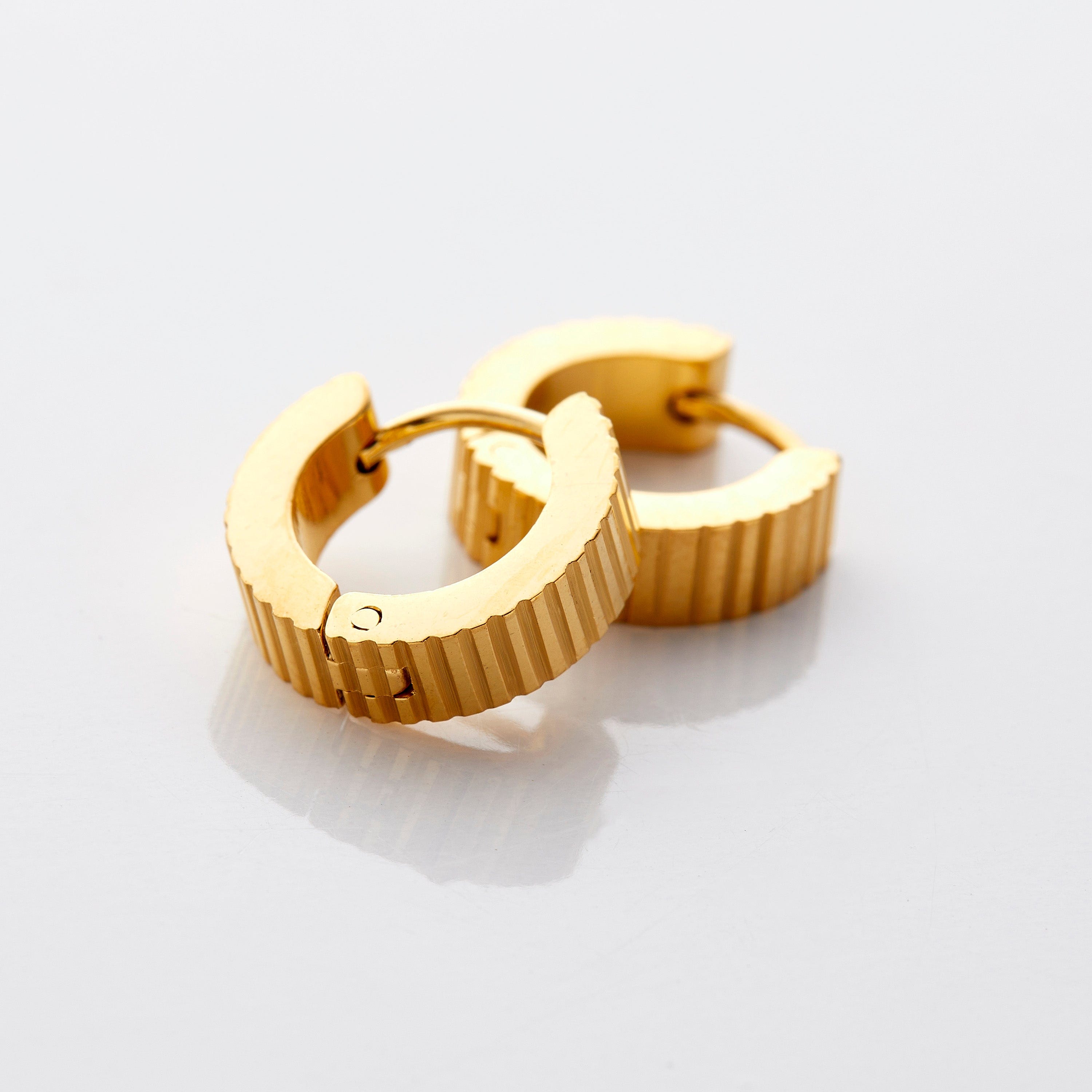 A pair of 18k gold plated hoop earrings that feature an array of ridges along the outer diameter of these small hugging earrings.